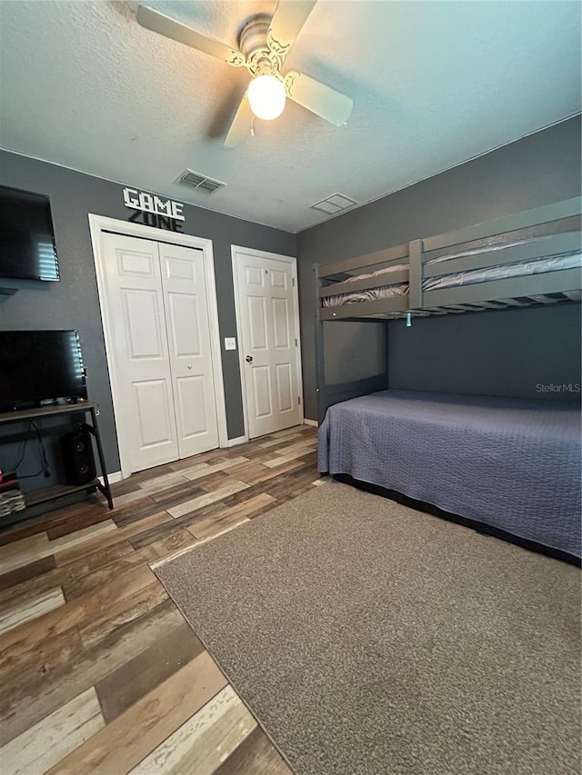 bedroom featuring a ceiling fan, visible vents, wood finished floors, baseboards, and a closet