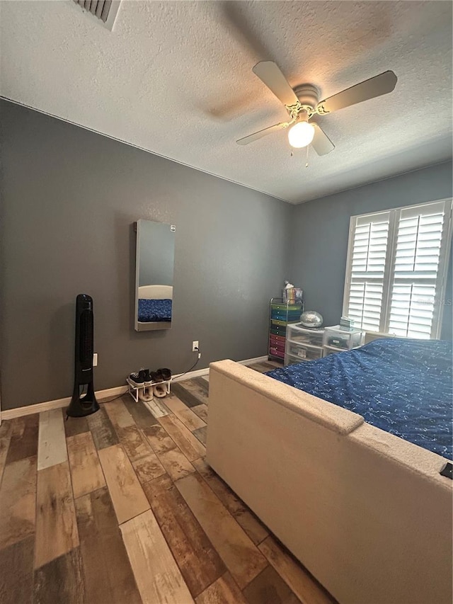 bedroom featuring a ceiling fan, a textured ceiling, visible vents, and hardwood / wood-style flooring