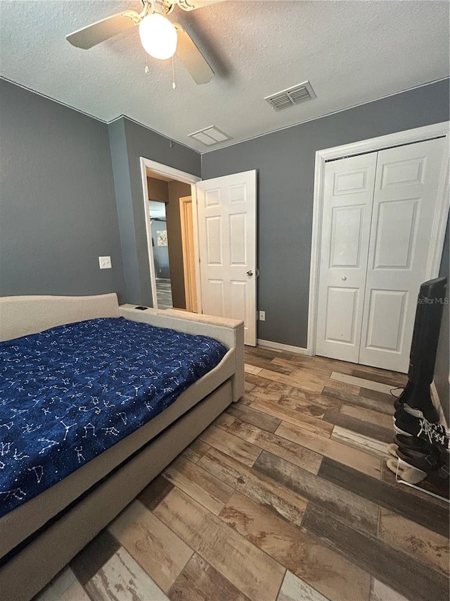 bedroom featuring ceiling fan, a textured ceiling, visible vents, and wood finished floors
