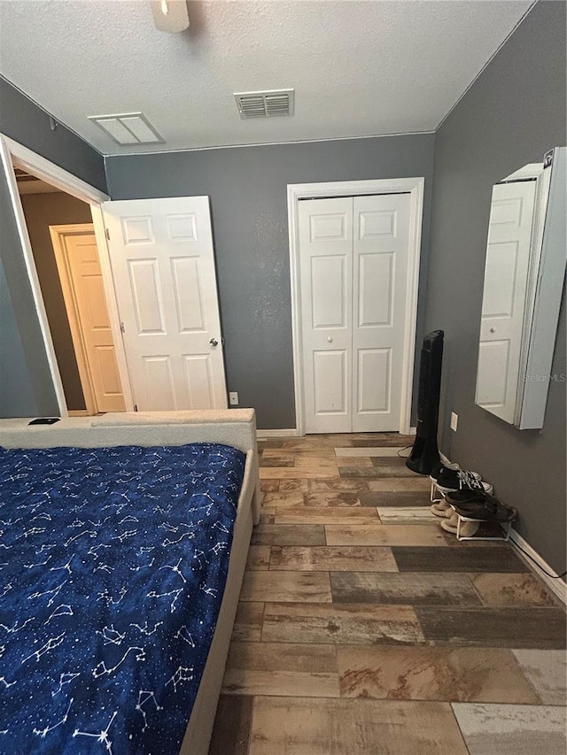 bedroom featuring ceiling fan, a textured ceiling, visible vents, wood finished floors, and baseboards