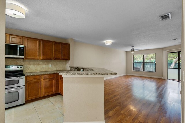 7449 Sugar Bend Dr Unit 7449, Orlando, FL 32819 - kitchen featuring appliances with stainless steel finishes, a peninsula, brown cabinetry, light wood finished floors, and open floor plan