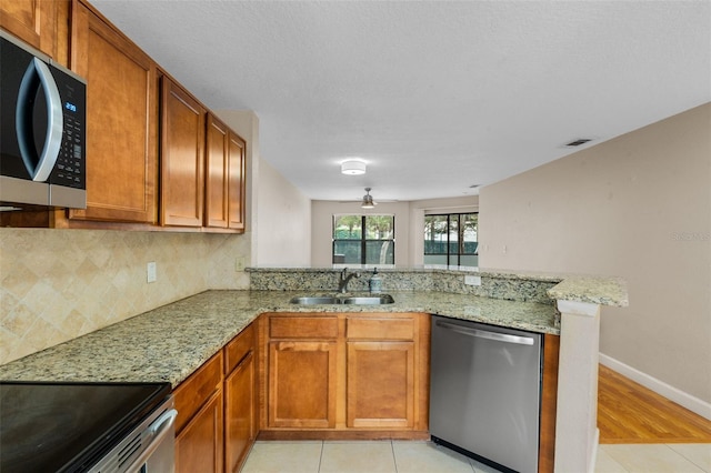 7449 Sugar Bend Dr Unit 7449, Orlando, FL 32819 - kitchen with stainless steel appliances, a sink, a peninsula, light stone counters, and brown cabinetry