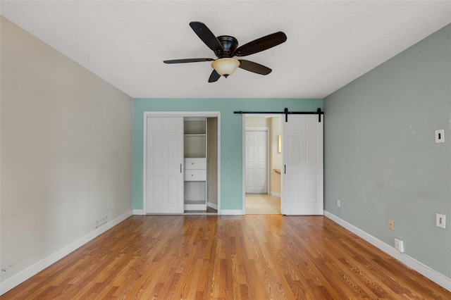 7449 Sugar Bend Dr Unit 7449, Orlando, FL 32819 - unfurnished bedroom featuring a barn door, light wood-type flooring, baseboards, and ceiling fan