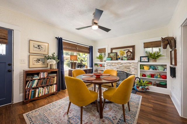 dining space featuring a textured ceiling, wood finished floors, a ceiling fan, and a stone fireplace