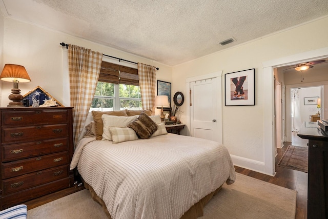 bedroom with baseboards, visible vents, a textured ceiling, and wood finished floors