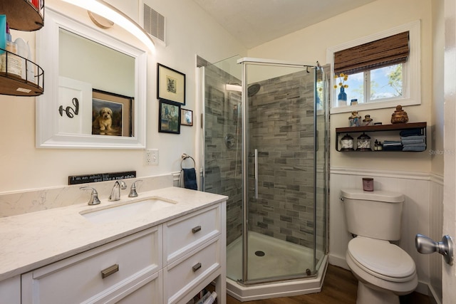bathroom with toilet, wood finished floors, a stall shower, visible vents, and vanity