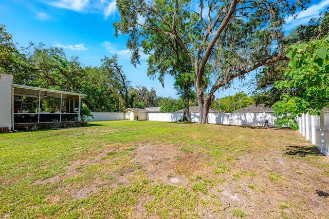 view of yard featuring an outbuilding, a sunroom, a storage shed, and a fenced backyard