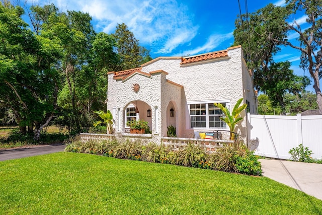 mediterranean / spanish-style home featuring stucco siding, a tiled roof, a front lawn, and fence