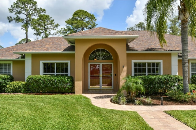 view of exterior entry featuring roof with shingles, stucco siding, and a yard