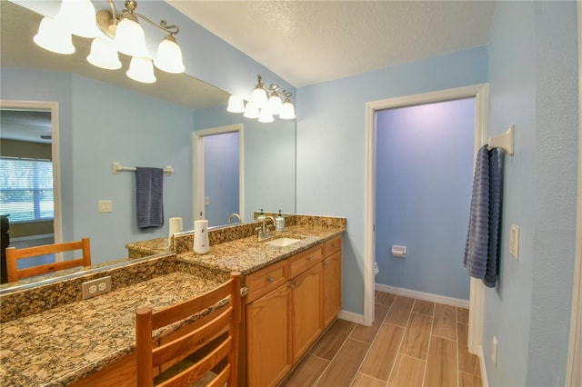 bathroom with wood tiled floor, baseboards, vanity, toilet, and an inviting chandelier