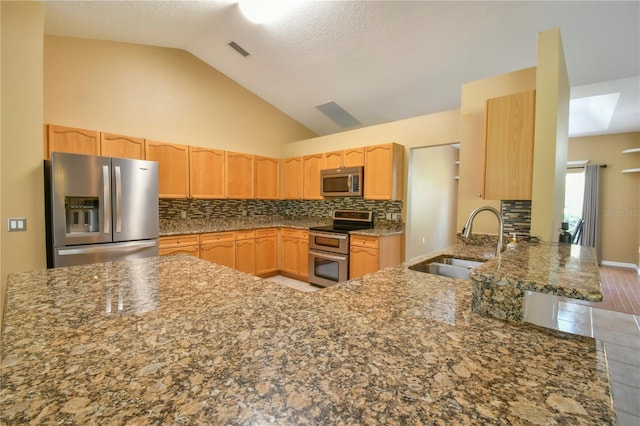 kitchen with a sink, light brown cabinetry, vaulted ceiling, and stainless steel appliances