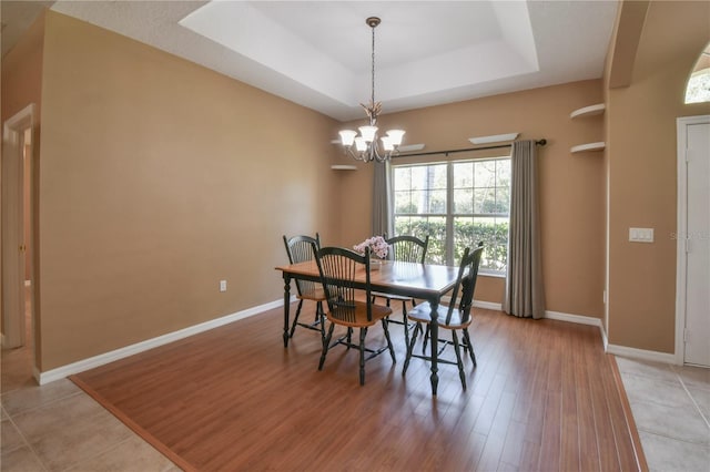 dining space featuring baseboards, an inviting chandelier, light wood-style flooring, and a raised ceiling