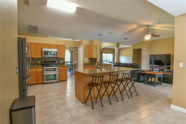 kitchen featuring appliances with stainless steel finishes, a sink, a kitchen breakfast bar, decorative columns, and decorative backsplash