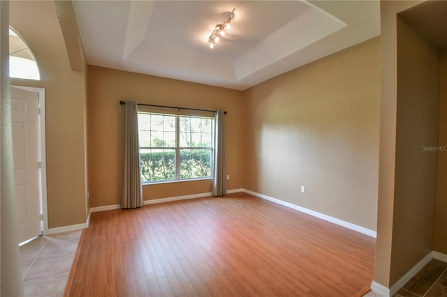 empty room with baseboards, light wood-style flooring, and a raised ceiling