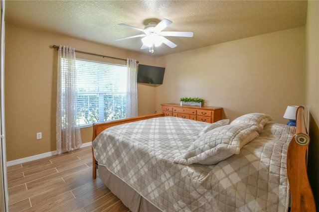 bedroom featuring a ceiling fan, a textured ceiling, baseboards, and light wood-type flooring