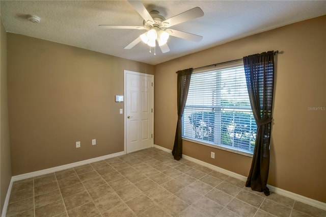 spare room with light tile patterned floors, ceiling fan, baseboards, and a textured ceiling