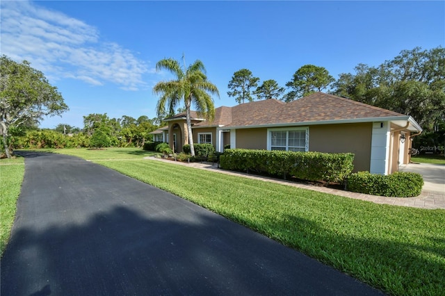 single story home featuring a front yard, stucco siding, a shingled roof, an attached garage, and driveway