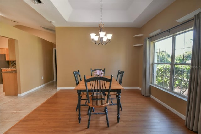 dining space with baseboards, a chandelier, light wood-style flooring, and a raised ceiling