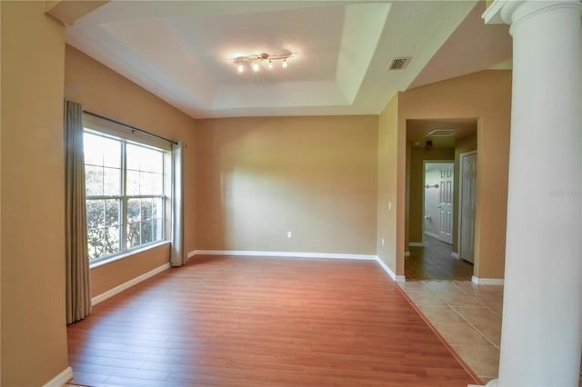 unfurnished room featuring visible vents, decorative columns, baseboards, a raised ceiling, and light wood-style flooring