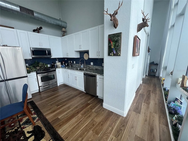 kitchen featuring a high ceiling, white cabinetry, tasteful backsplash, a sink, and appliances with stainless steel finishes