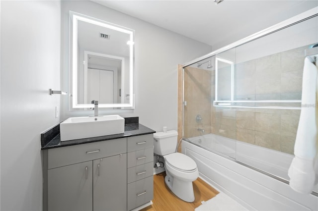 full bathroom with visible vents, vanity, wood finished floors, shower / bath combination with glass door, and toilet