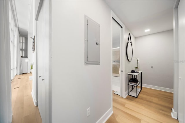 hall with light wood-type flooring, baseboards, and electric panel