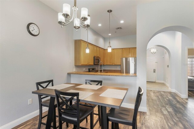 dining space featuring arched walkways, wood finished floors, baseboards, a chandelier, and a high ceiling