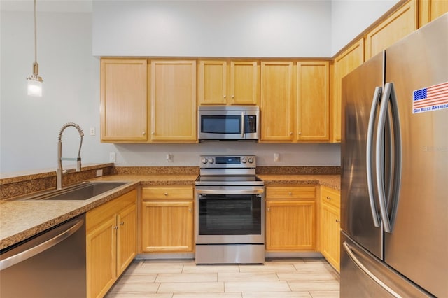 kitchen featuring appliances with stainless steel finishes, a sink, light brown cabinetry, wood tiled floors, and pendant lighting