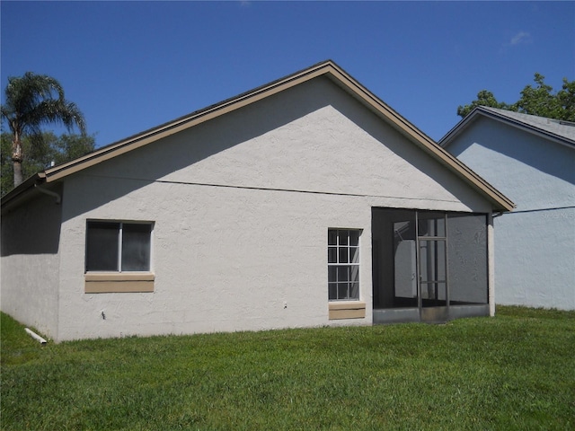 back of property with a yard, stucco siding, and a sunroom