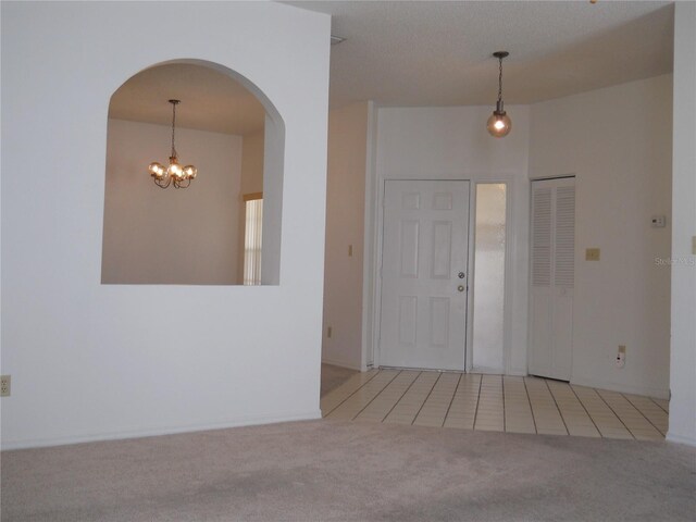 carpeted foyer with an inviting chandelier, arched walkways, and tile patterned floors