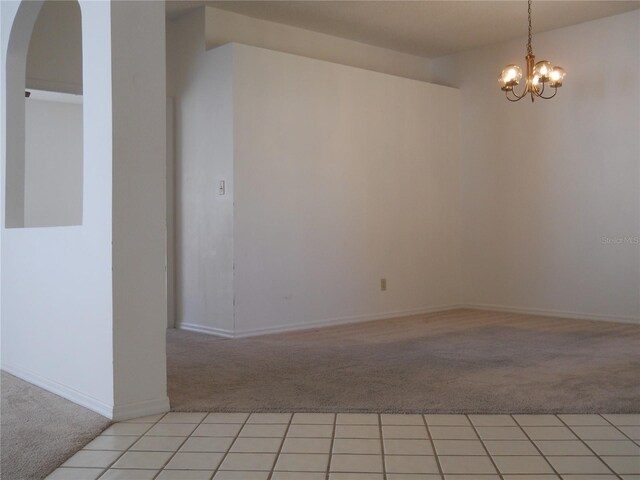 spare room featuring light colored carpet, arched walkways, and a notable chandelier