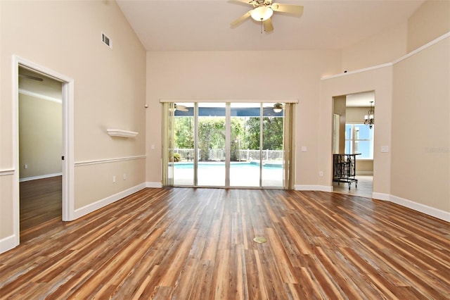 unfurnished room with baseboards, a towering ceiling, ceiling fan with notable chandelier, and wood finished floors