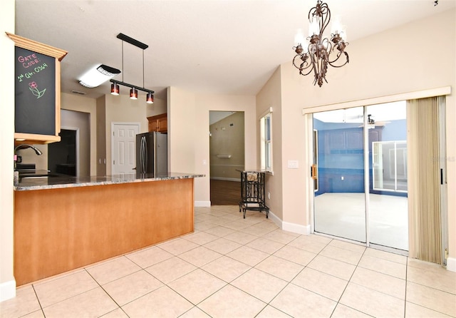 kitchen featuring an inviting chandelier, freestanding refrigerator, a peninsula, light tile patterned flooring, and stone countertops