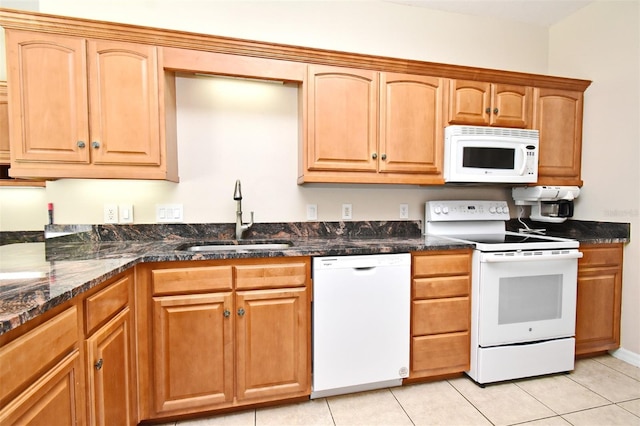 kitchen featuring a sink, light tile patterned floors, dark stone countertops, and white appliances