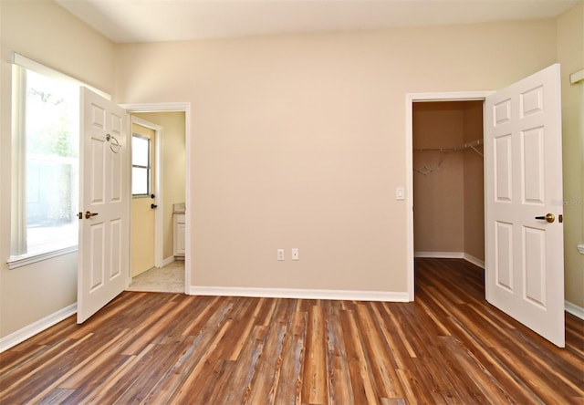 unfurnished bedroom featuring baseboards, a spacious closet, wood finished floors, and a closet