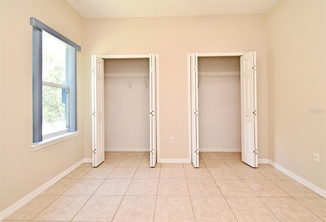 unfurnished bedroom featuring baseboards, multiple closets, light tile patterned flooring, and multiple windows