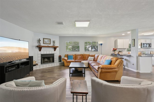 living room featuring a tiled fireplace, a textured ceiling, wood finished floors, and visible vents