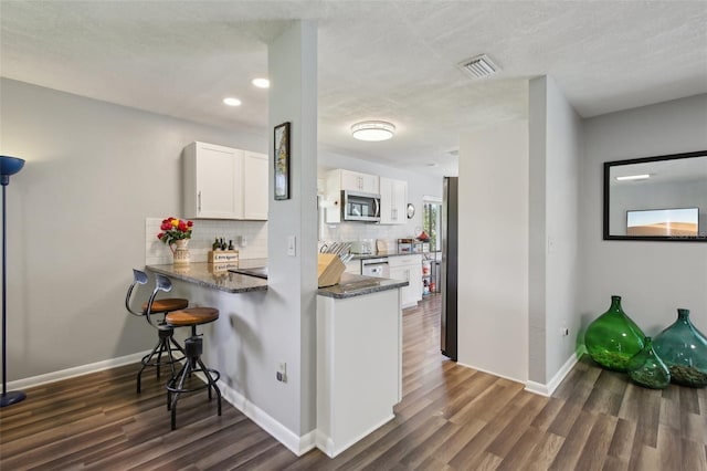 kitchen featuring visible vents, appliances with stainless steel finishes, tasteful backsplash, white cabinets, and dark wood-style floors