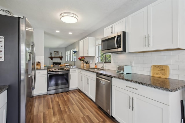 kitchen with white cabinetry, appliances with stainless steel finishes, a sink, and dark stone countertops