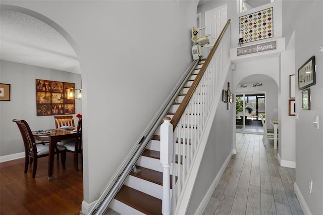 staircase featuring baseboards, arched walkways, a high ceiling, and wood finished floors