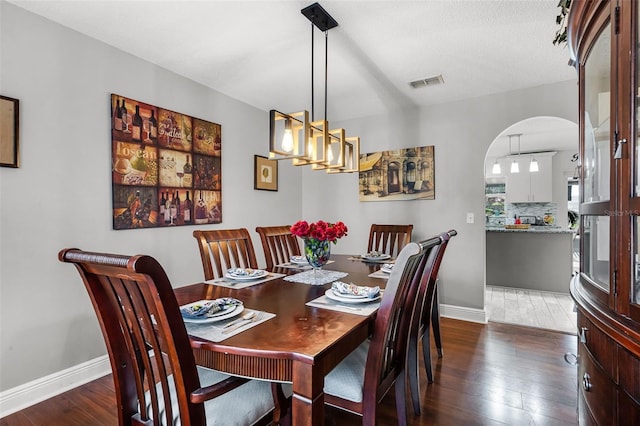 dining room featuring visible vents, arched walkways, baseboards, and dark wood-type flooring