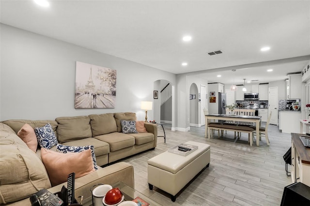 living room featuring light wood finished floors, arched walkways, recessed lighting, baseboards, and visible vents