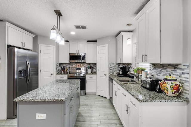 kitchen featuring a sink, light stone counters, stainless steel appliances, and white cabinetry