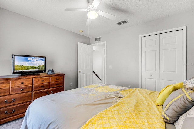 bedroom with a textured ceiling, ceiling fan, visible vents, and a closet