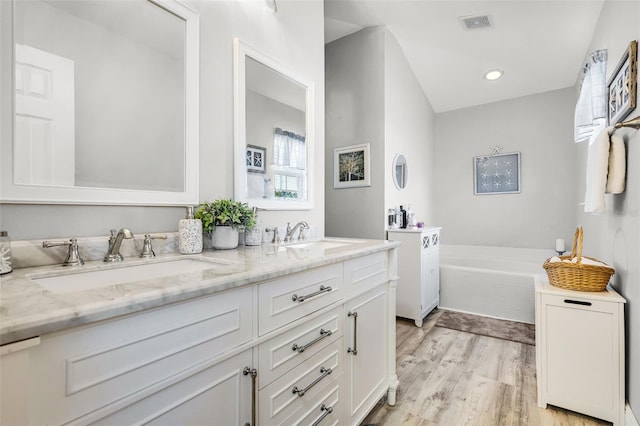 bathroom featuring a sink, a bath, double vanity, and wood finished floors