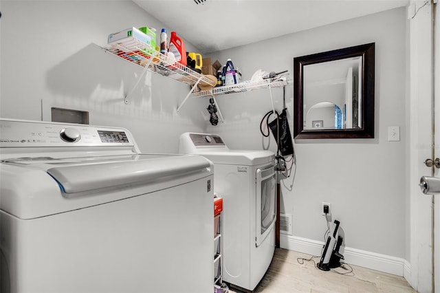 clothes washing area with washer and dryer, laundry area, baseboards, and light wood-type flooring