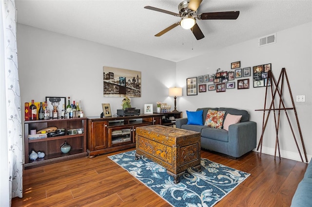 living area with a ceiling fan, a textured ceiling, visible vents, wood finished floors, and baseboards