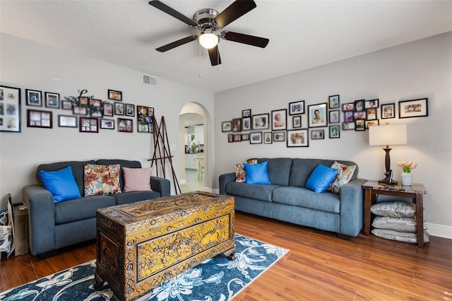 living area featuring visible vents, a ceiling fan, wood finished floors, a textured ceiling, and arched walkways
