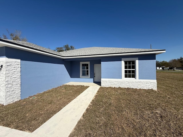 view of front of home featuring stucco siding, a front lawn, and stone siding