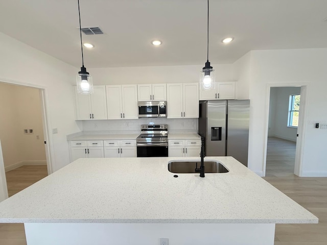 kitchen with white cabinets, a sink, stainless steel appliances, baseboards, and light wood-type flooring